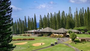 Un campo de golf con un club de campo, una zona de estacionamiento y vista al océano.