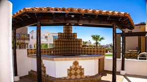 A covered outdoor area with a tiled floor, a central counter, and a pergola structure. - Casa Costa Diamante F27 (Puerto Peñasco)