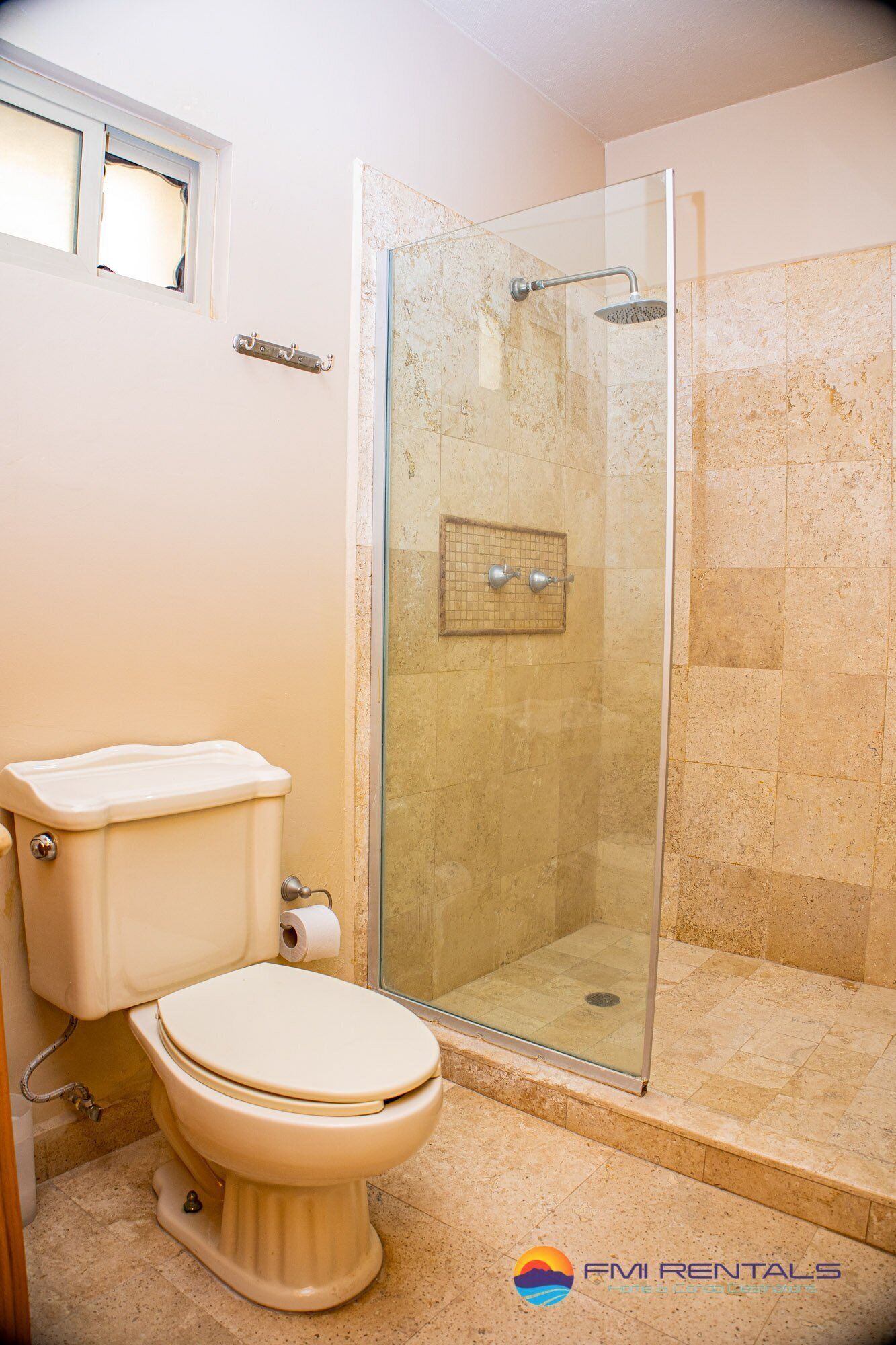 A bathroom with a toilet, a glass-enclosed shower, and beige tiled walls.