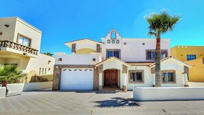A modern two-story house with a white facade, a central entrance with a wooden door, and a small balcony on the upper floor. - Casa Costa Diamante F27 (Puerto Peñasco)