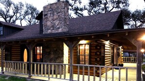 A log cabin with a stone chimney, wooden deck, and a railing. - Hotel luxury in a Log Cabin (Rockport)
