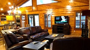 A log cabin interior with a living room featuring leather sofas, a television, and a dining area with wooden cabinets and a chandelier. - Hotel luxury in a Log Cabin (Rockport)