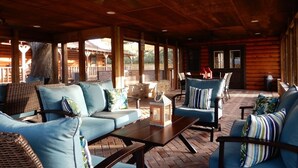 A covered outdoor seating area with wicker furniture and blue cushions, a brick floor, and wooden walls. - Hotel luxury in a Log Cabin (Rockport)