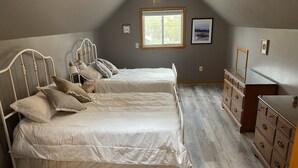 A bedroom with two beds, a dresser, a window, and a painting on the wall.