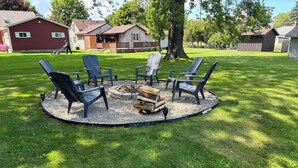 A circular seating area with four Adirondack chairs around a fire pit, surrounded by a gravel ring.