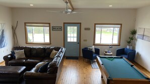 A room with a pool table, a leather sofa, and two armchairs.
