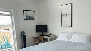 Une chambre à coucher avec un lit, un bureau avec un ordinateur, une chaise et une fenêtre.