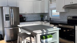 Une cuisine moderne avec des meubles blancs, un réfrigérateur en acier inoxydable, un four encastré et un îlot central doté de tabourets.