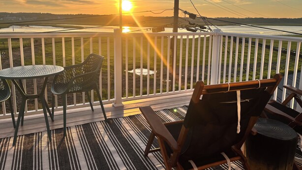 Une terrasse avec une table et des chaises, donnant sur un paysage illuminé par le coucher du soleil.