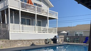 Une piscine dotée d’une rambarde de sécurité en métal, un espace patio avec une table et des chaises, et une maison avec un balcon en arrière-plan.