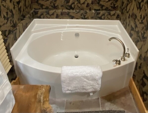 Una bañera rectangular con una toalla blanca al lado, un taburete de madera y un piso de baldosas.