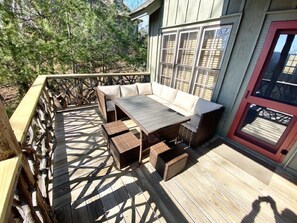 Una terraza de madera con una mesa, sillas y un banco acolchado, además de una puerta con ventanal.