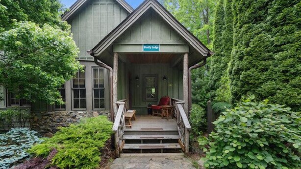 Une véranda en bois avec une enseigne indiquant « Firefly Lodge », des marches en pierre et un banc.