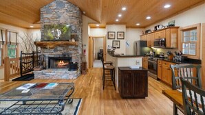 Un vaste espace de vie doté d’une cheminée en pierre, d’un plafond en bois et d’une cuisine avec des armoires et des appareils électroménagers en bois.