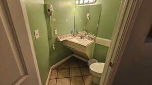 Et lille badeværelse med grøn væg, hvid vask, et spejl og et toilet.
