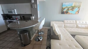 A modern kitchen with a granite countertop, white bar stools, and a white leather sofa.