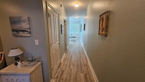 A hallway with wooden flooring, a lamp, a decorative bowl, and a painting on the wall.