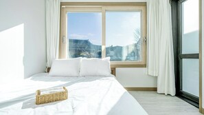 A bedroom with a large bed, a window with curtains, and a view of buildings.