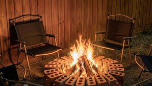 A circular fire pit with logs and bricks arranged around it, surrounded by two folding chairs.