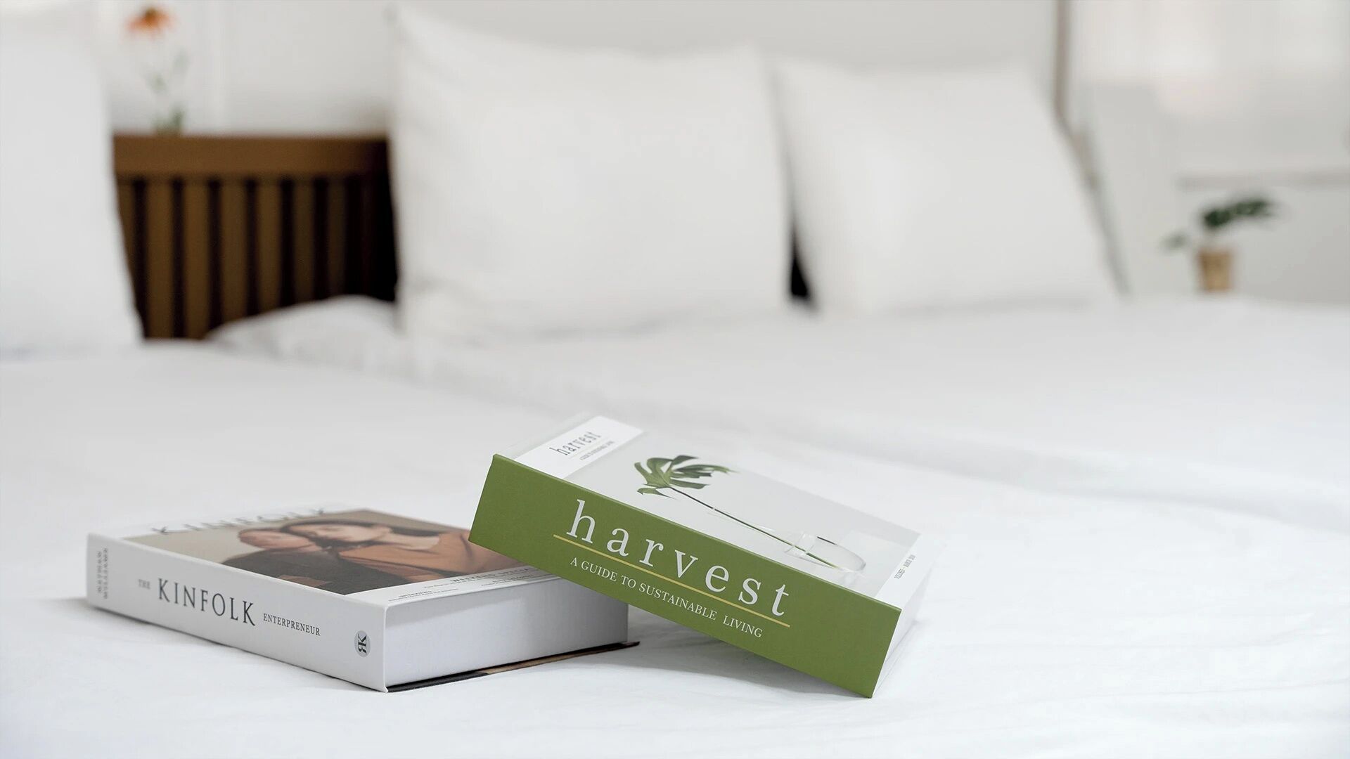 A neatly made bed with a book titled 'harvest' and another book titled 'The Kinfolk Entrepreneur' on it.