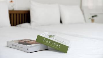 A neatly made bed with a book titled 'harvest' and another book titled 'The Kinfolk Entrepreneur' on it.