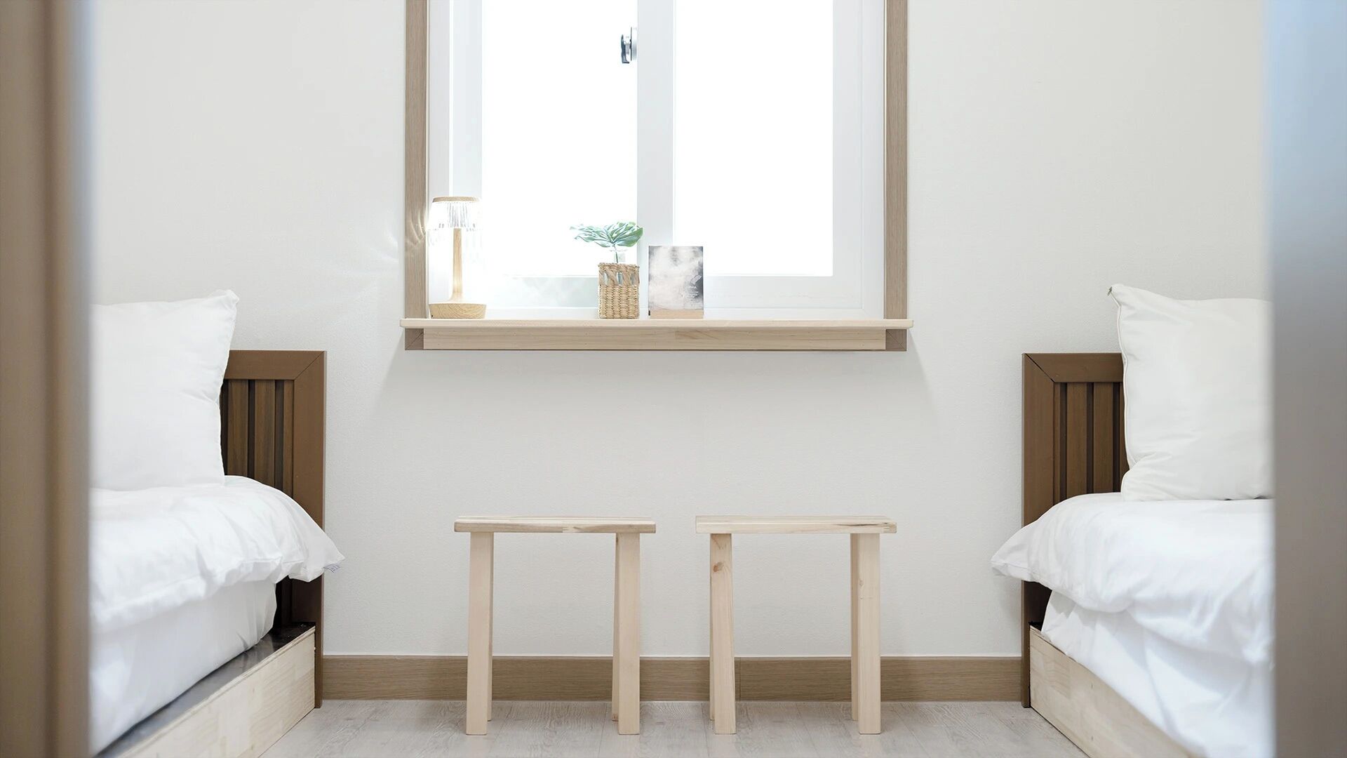A bedroom with two beds, a window, and two small wooden tables.