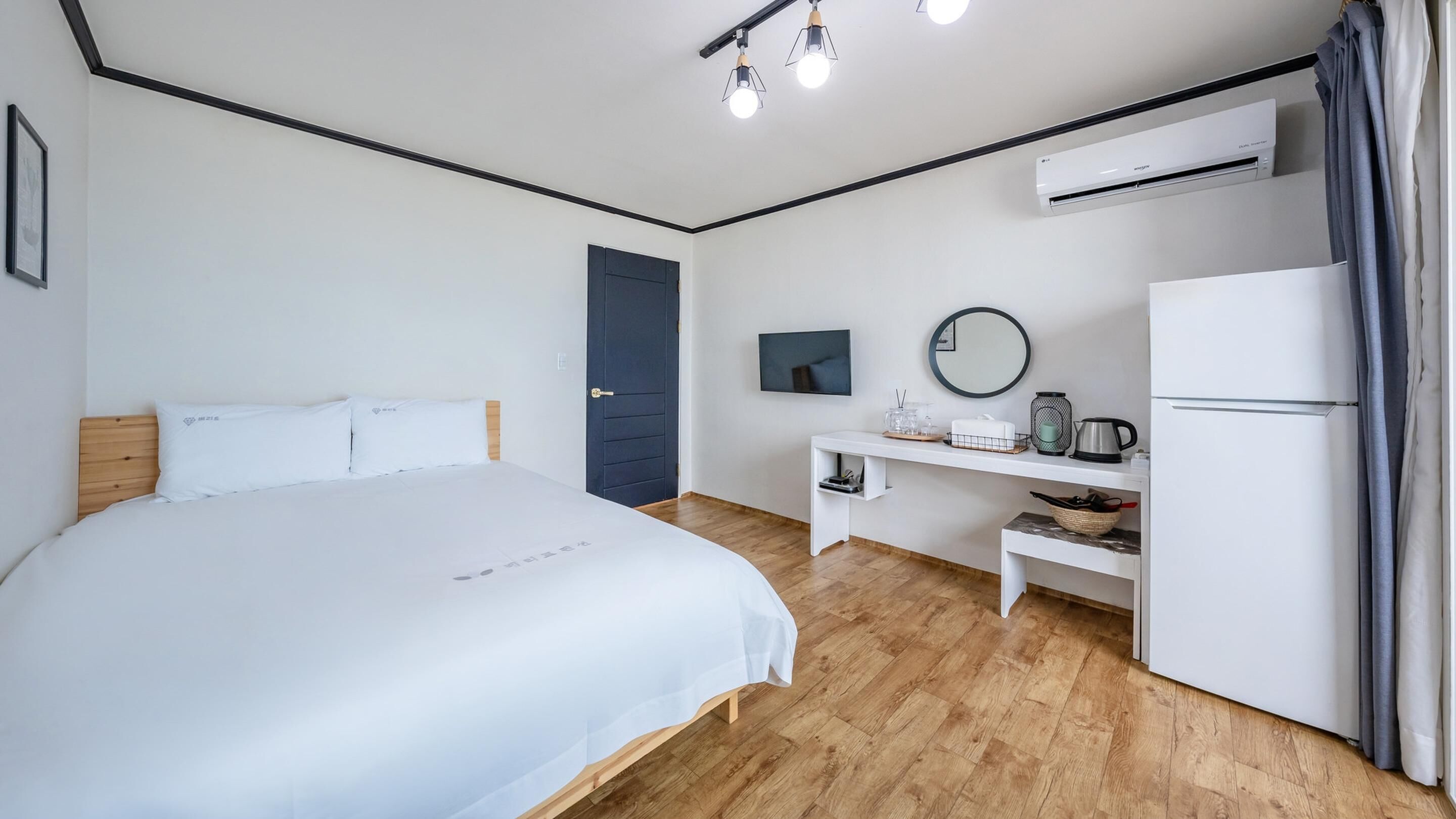 Une chambre d’hôtel équipée d’un lit, d’un bureau, d’une télévision, d’un miroir, d’un climatiseur et d’un réfrigérateur.