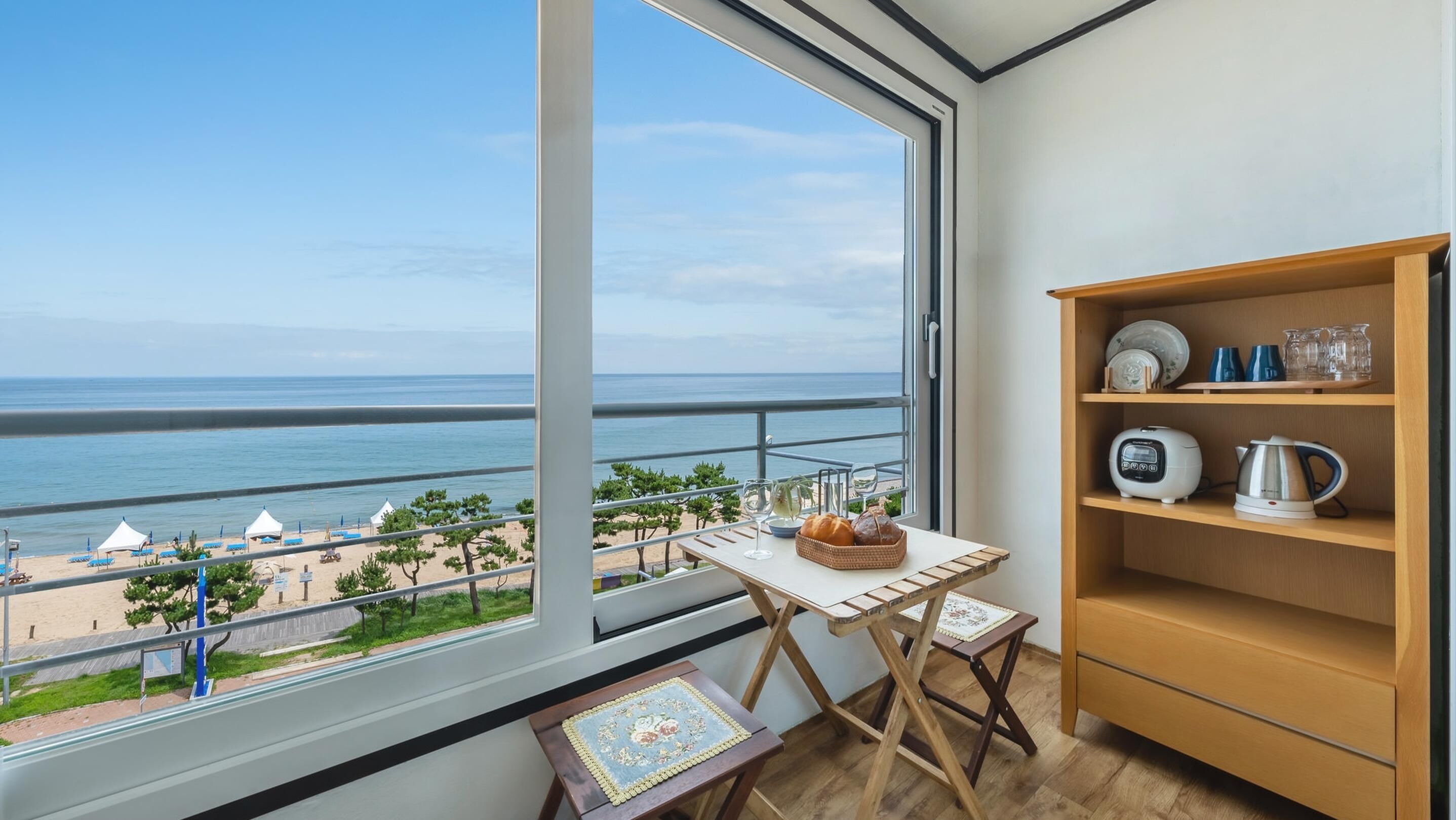 Ein Balkon mit Meerblick, ein kleiner Tisch mit einem Brotkorb und eine Ablage mit Küchenutensilien.