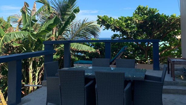 An outdoor patio with wicker furniture, a blue railing, and lush greenery. - HIDDEN TREASURE (Point Blanche)