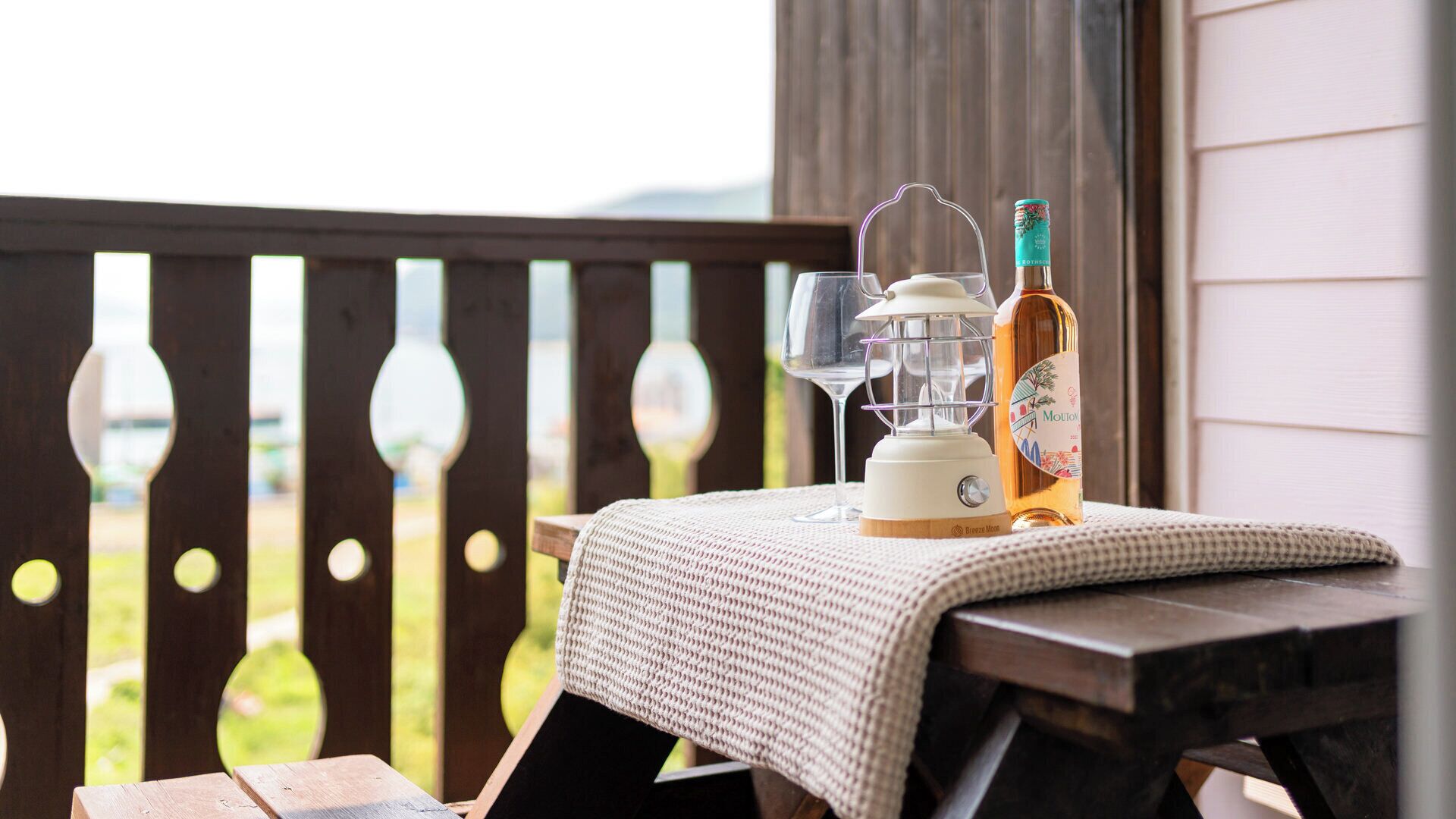 A wooden deck with a table covered by a white cloth, a bottle of Moutai, a candle, and a glass.