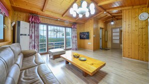 A wooden interior with a sofa, a wooden table, and a large window with curtains. - Geoje Gaonara Pension (Geoje)