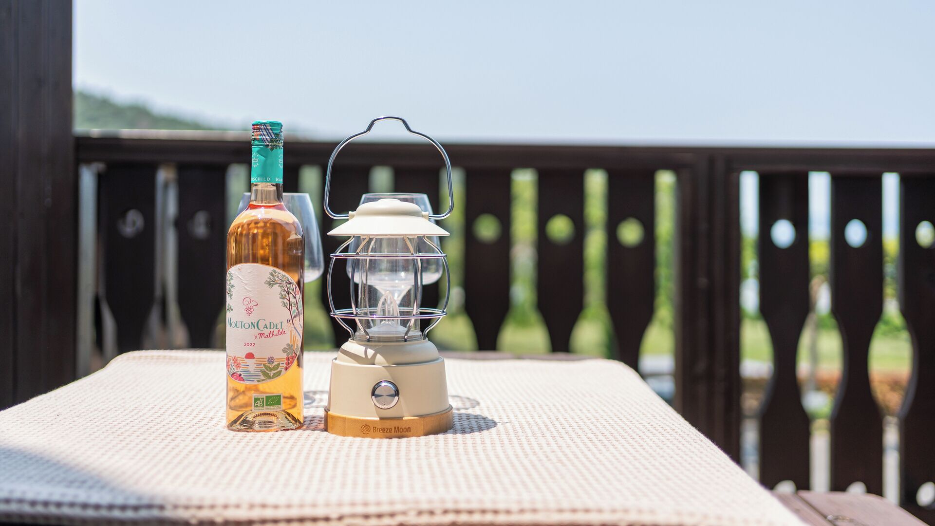 A bottle of alcohol and a lantern on a textured surface outdoors.