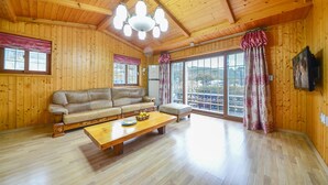 A wooden-paneled room with a sofa, a coffee table, and a large window. - Geoje Gaonara Pension (Geoje)