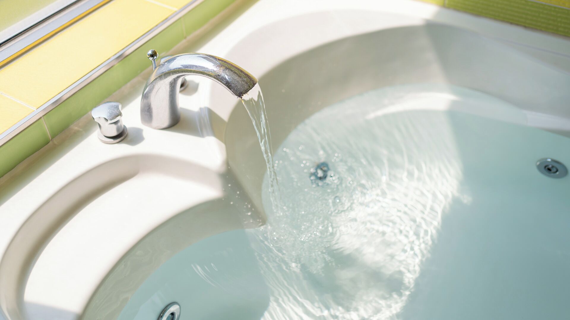 A bathtub with running water, a chrome faucet, and a green tiled wall.