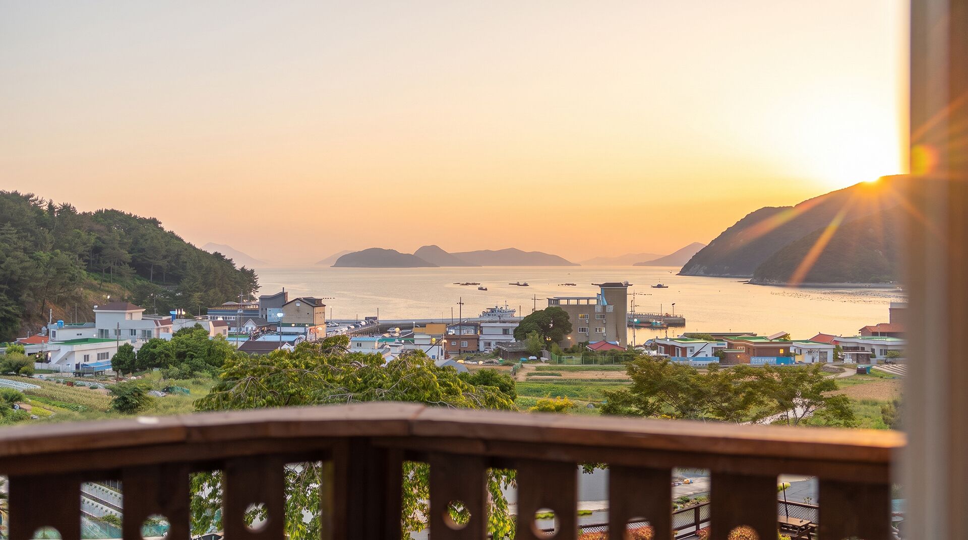 A coastal town with a view of the sea and hills, featuring buildings and a dock.