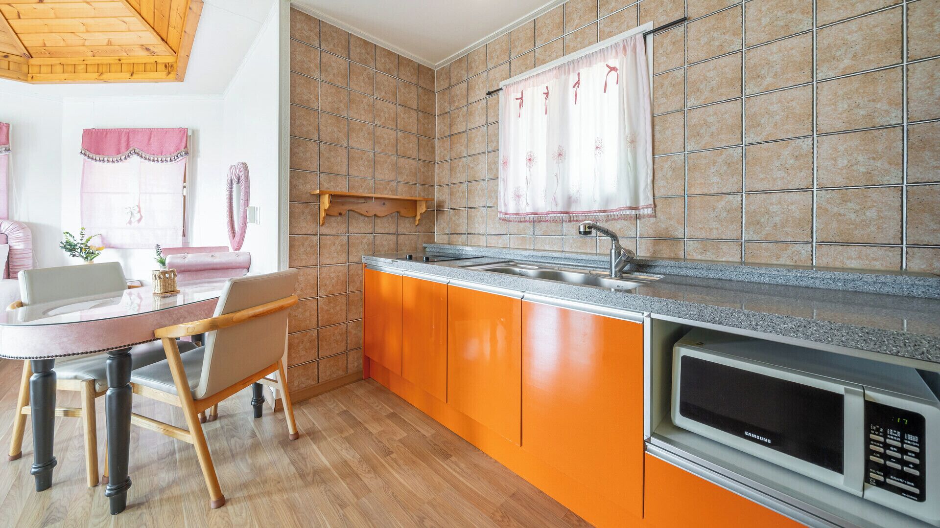 A kitchen with orange cabinets, a stainless steel sink, and a Samsung microwave.