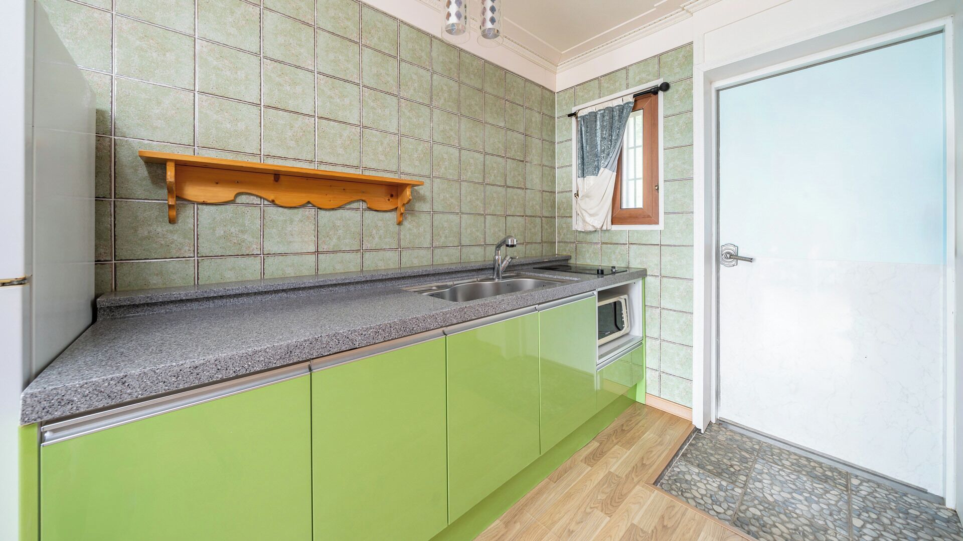 A kitchen with green cabinets, a granite countertop, a built-in oven, and a wooden shelf.