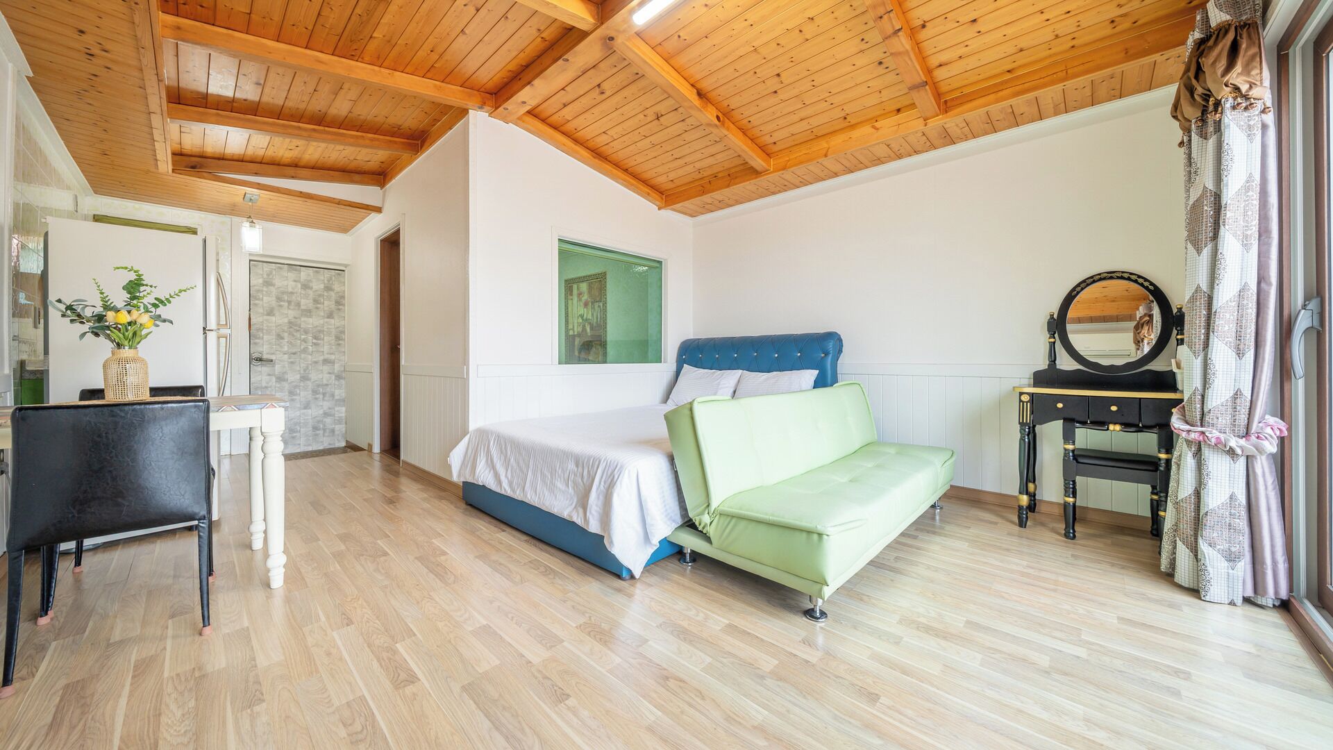 A bedroom with a bed, a green sofa, a small table, and a mirror.