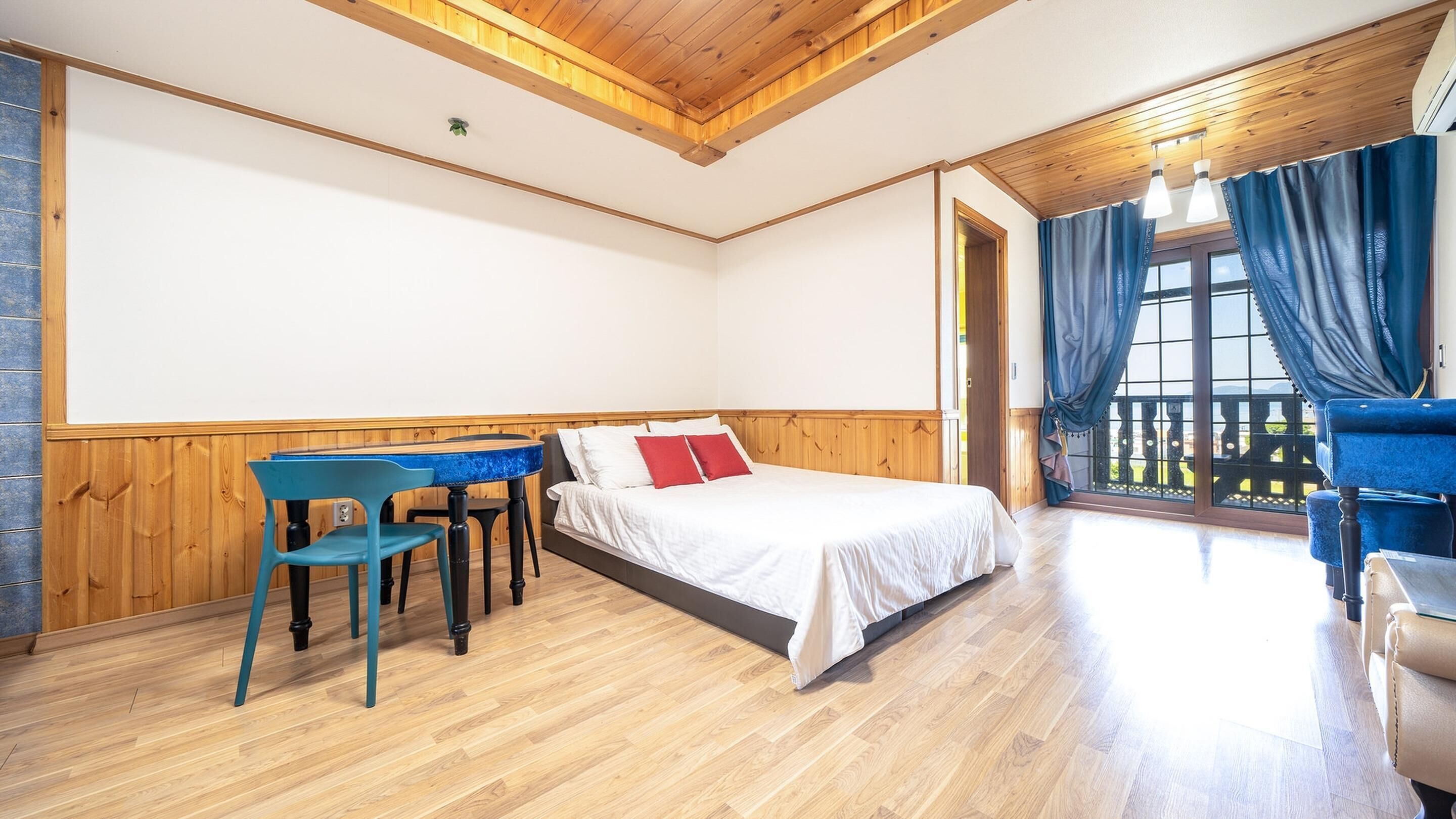 A room with a bed, a table with chairs, and a balcony with curtains.