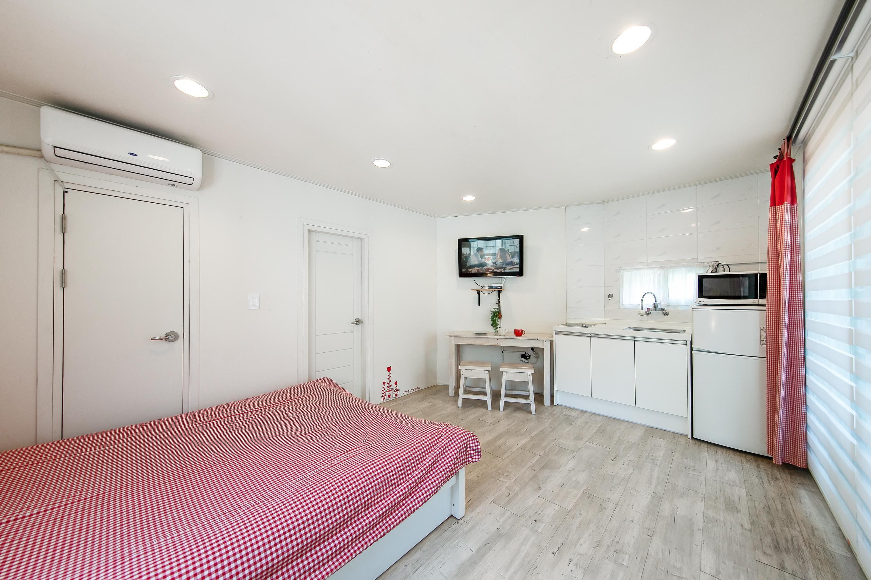 A compact room with a bed, kitchenette, and a TV mounted on the wall.