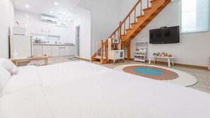 A modern, well-lit room with a large bed, a kitchen area, and a staircase.