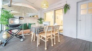 A covered patio with a dining table and chairs, a grill, and umbrellas.