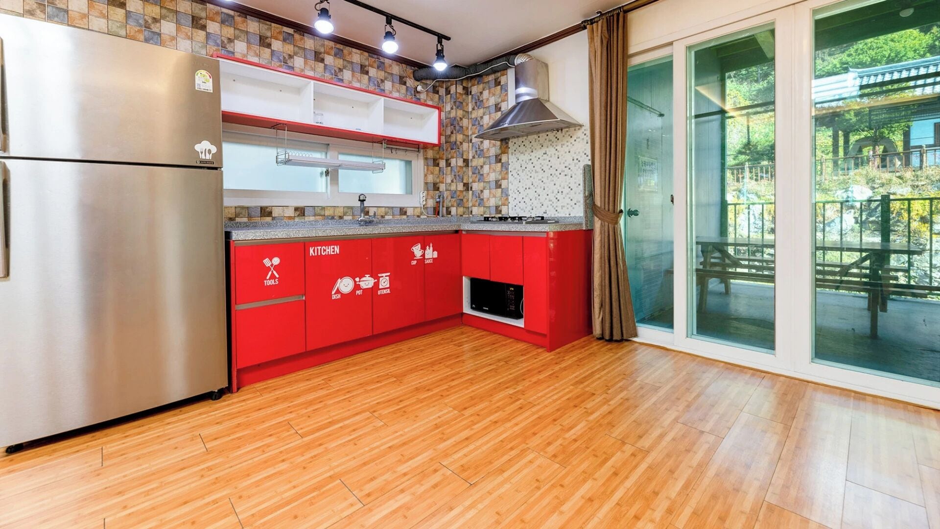 A kitchen with red cabinets, a stainless steel refrigerator, and a view of a patio through glass doors.