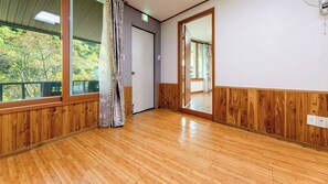 A room with wooden flooring, a large window with a view of trees, and a door leading to another room. - Gapyeong Yeoul Kids Pension (Gapyeong)