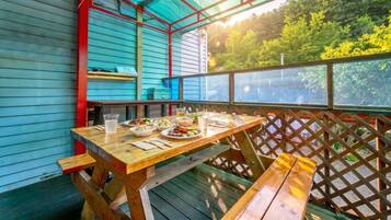 An outdoor dining area with a wooden table and benches, surrounded by a wooden fence and a view of trees.