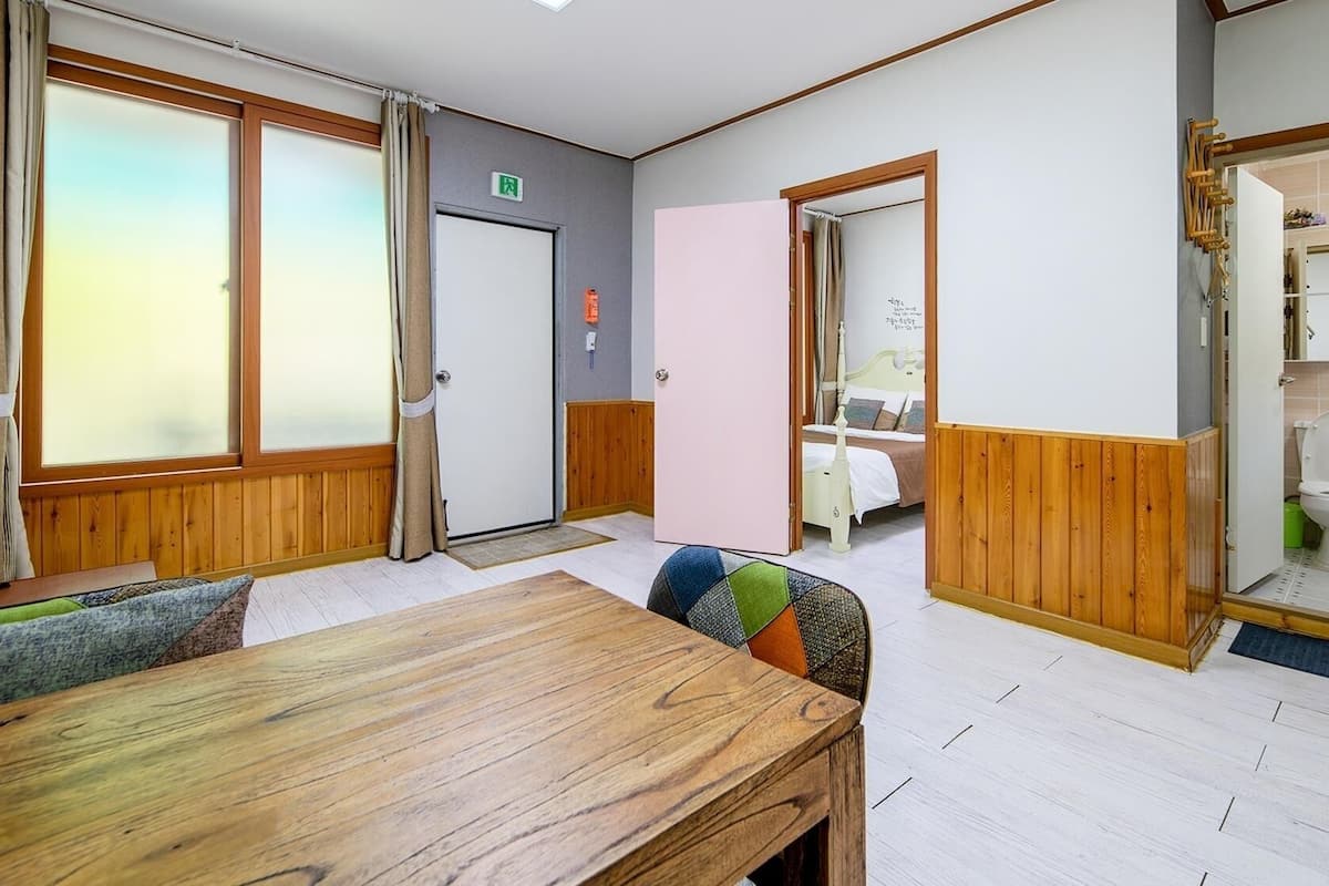 A hotel room with a wooden floor, a dining table, a bed, and a bathroom.