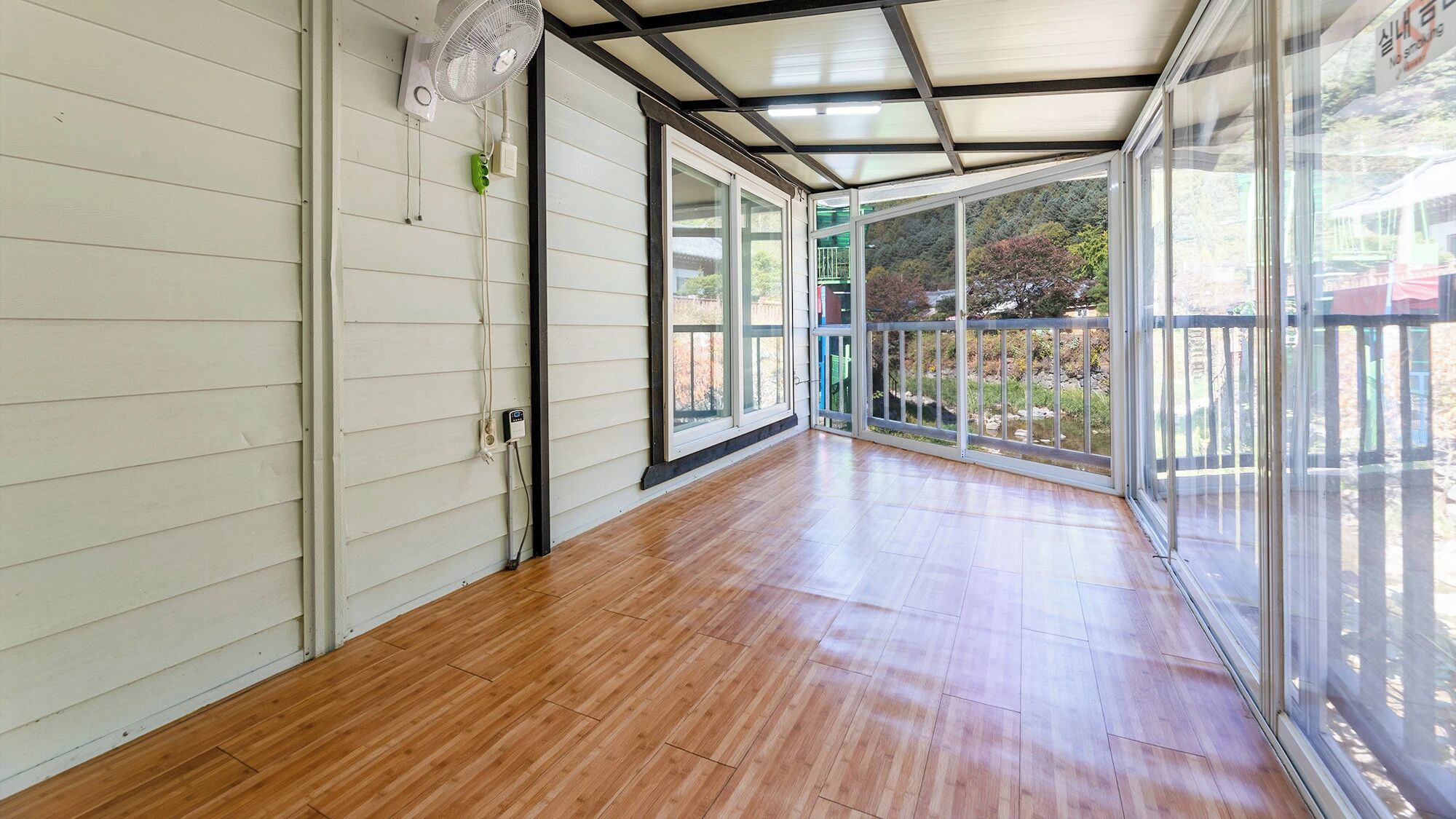 A corridor with wooden flooring, a ceiling fan, and large windows.