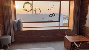 A cozy room with a large window, a wooden bench, a small table, and a cushioned seat. - Jeju Sunjinhanga Pension (Seogwipo)