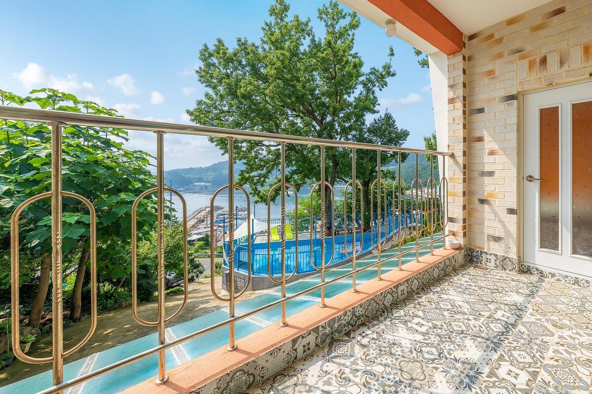 A balcony with a metal railing overlooking a swimming pool and a scenic view of trees and hills.