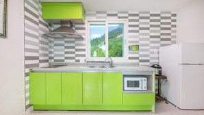 A kitchen with green cabinets, a built-in microwave, and a window with a view of greenery. - Tongyoung Blue House Spa Pension (Tongyeong)